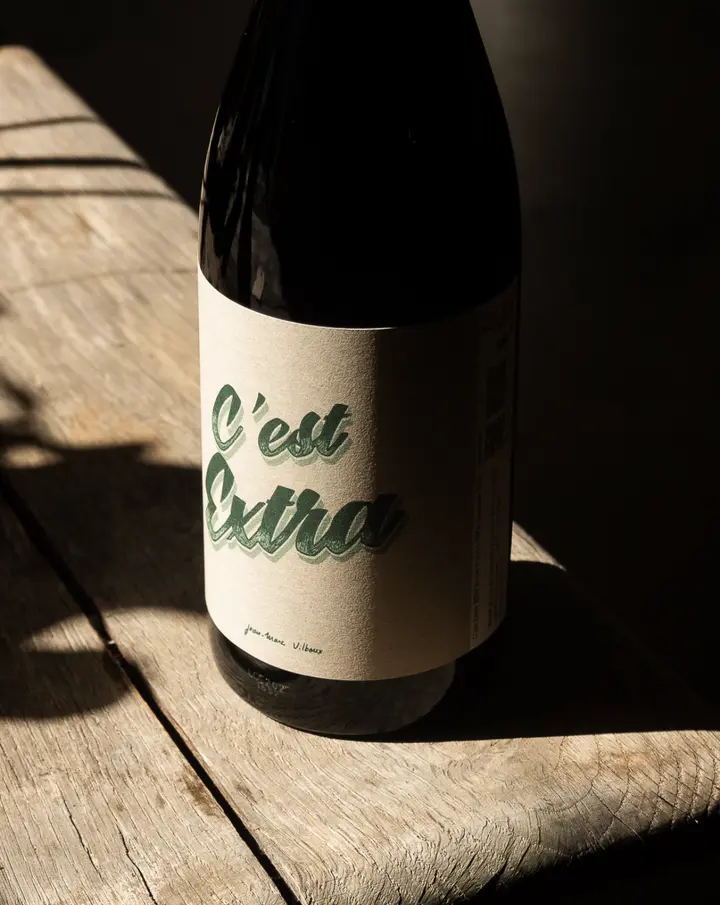 Une bouteille C’est Extra de Jean-Marie Vilboux dans la lumière sur une table en bois
