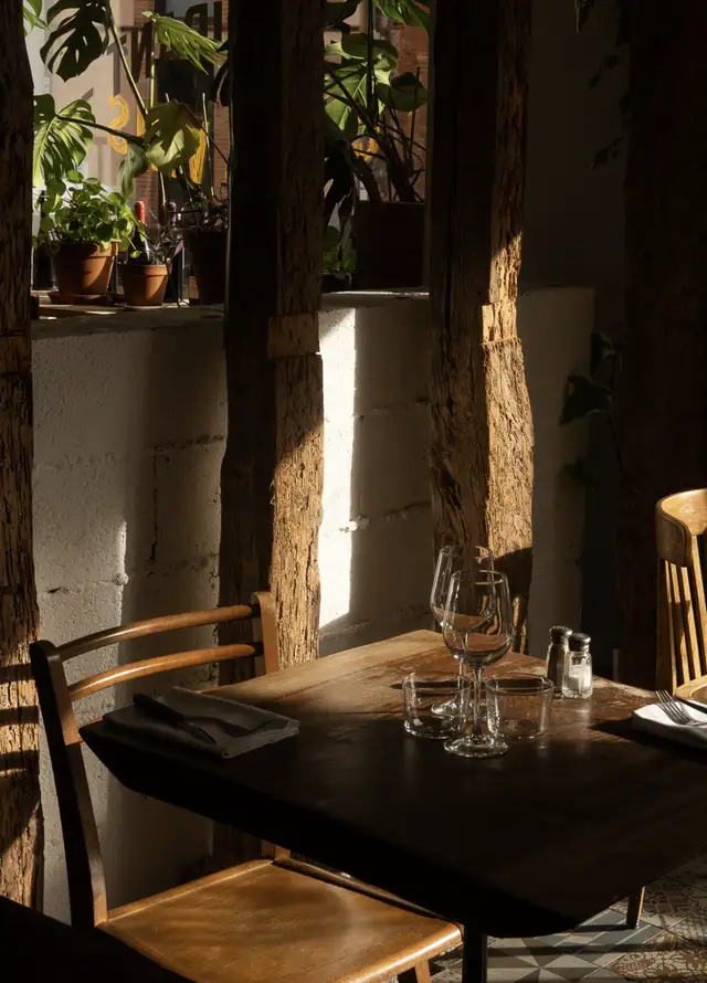 La salle au soleil, une table dressée entre les poutres et les plantes